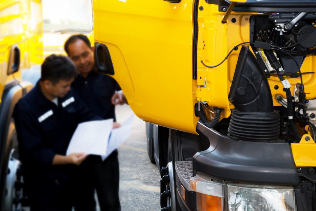 Two mechanics checking a yellow truck for maintenance