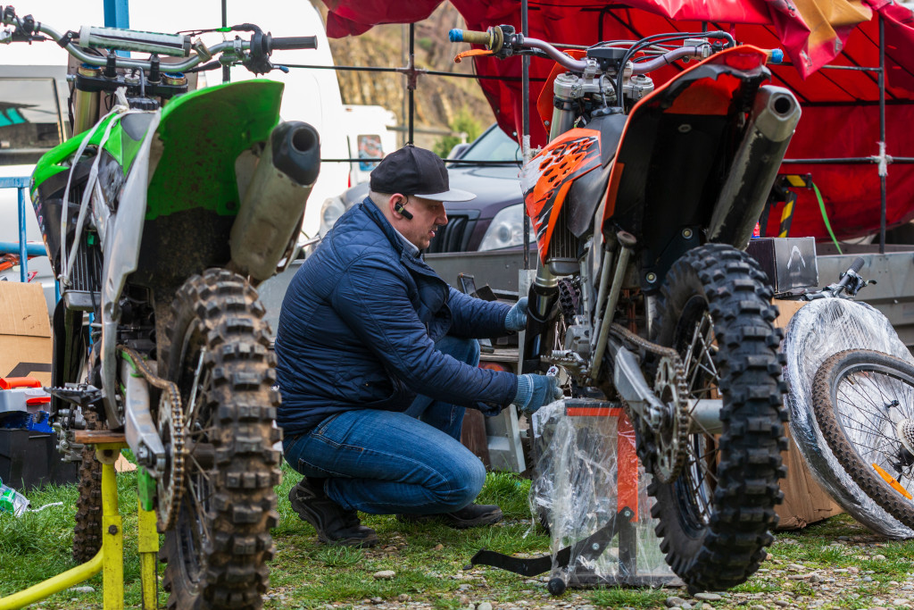 A business owner and mechanic repairing two dirt bikes on paddock stands while at a motocross rally