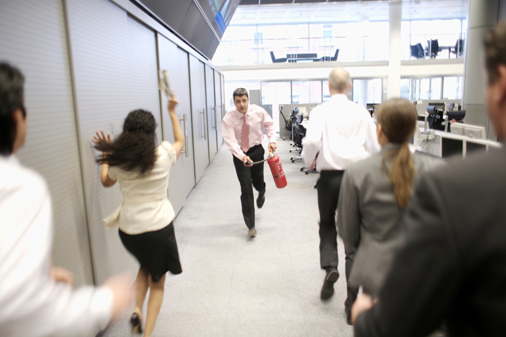 Businessman running with fire extinguisher while employees run the opposite direction